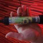 Een hand houdt een wegwerp-vape van Bang vast met het opschrift "36.000 trekjes, dubbele appel" met een groen ontwerp van een wezen met scherpe tanden.