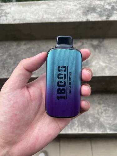 A person holds a gradient-colored vape device with "18,000 puffs" and "Triple Berry Ice" written on it.