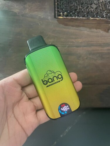 A hand holding a green and yellow gradient Bang disposable vape device with a digital screen displaying battery charge and colored lights.