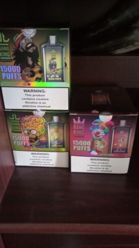 Trois boîtes de vapes jetables Bang King, chacune étiquetée « 15 000 PUFFS » et présentant des graphismes de personnages différents, disposées sur une étagère avec des avertissements concernant la nicotine sur l'emballage.