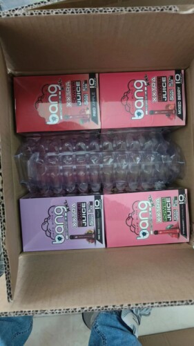 Een open kartonnen doos met vier verpakkingen met wegwerp-vape-apparaten van Bang, met smaken als Red Apple, Mixed Berry en Strawberry Watermelon, samen met wat plastic verpakkingsmateriaal.