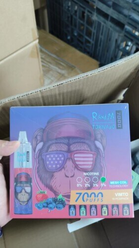 Une personne tient une boîte de vapes jetables RandM Tornado 7000 bouffées, avec des saveurs de baies et une variante Vimto, emballées dans une boîte en carton avec des informations visibles sur la technologie des bobines en maille.